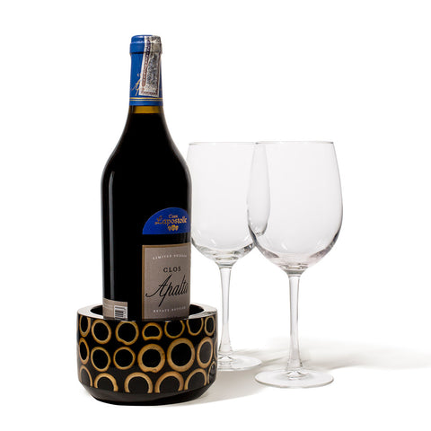 handmade light brown bamboo rings on black wood rounded wine bottle coaster with wine bottle and two glasses