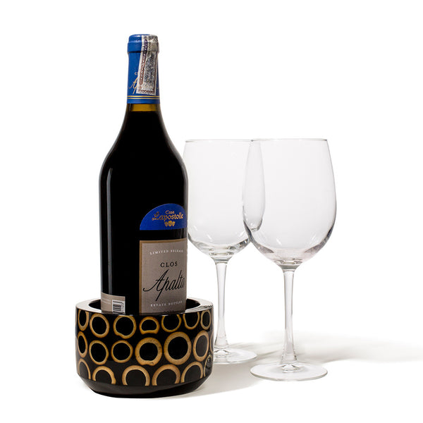 handmade light brown bamboo rings on black wood rounded wine bottle coaster with wine bottle and two glasses